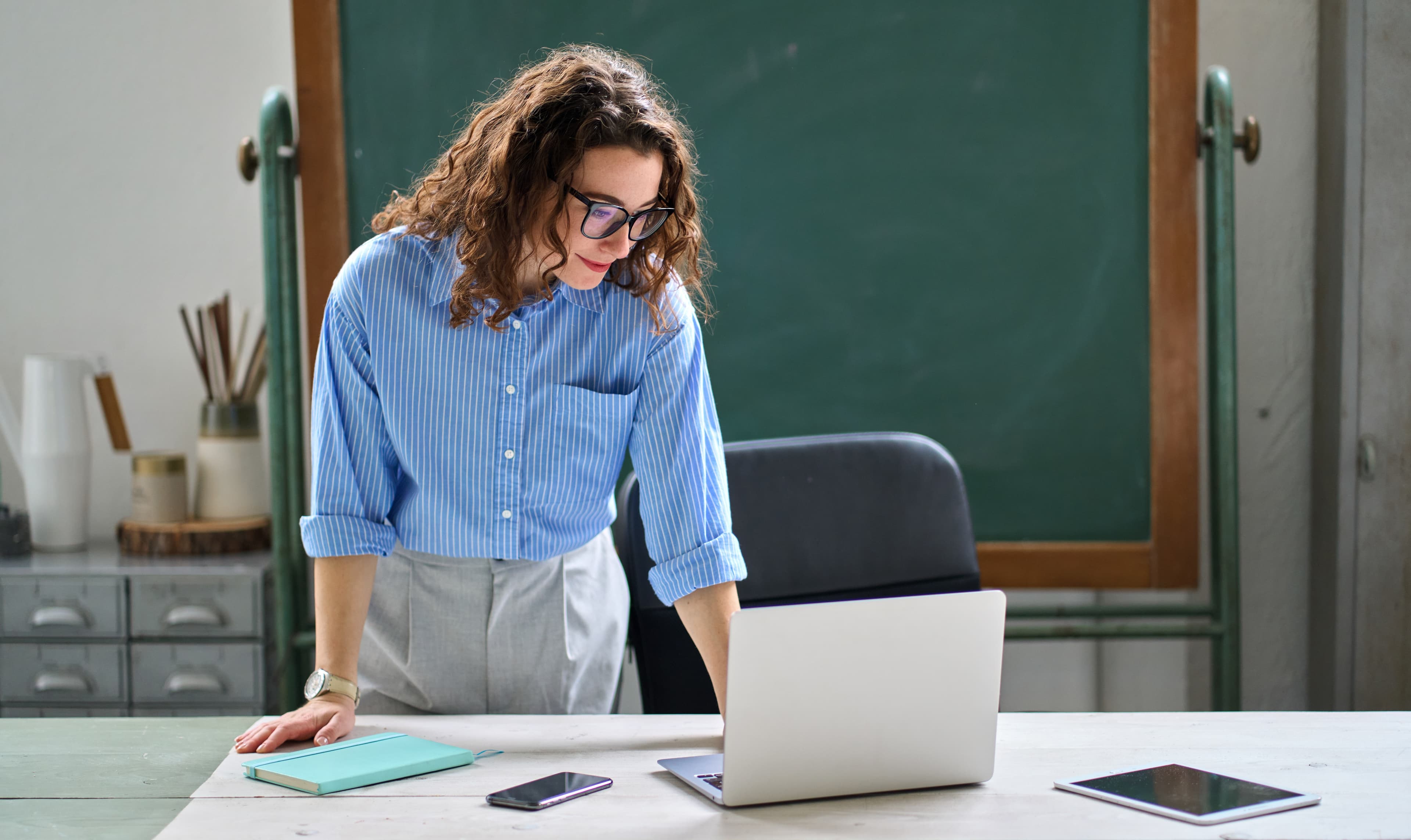Teacher reviewing literacy learning progress on laptop at classroom desk